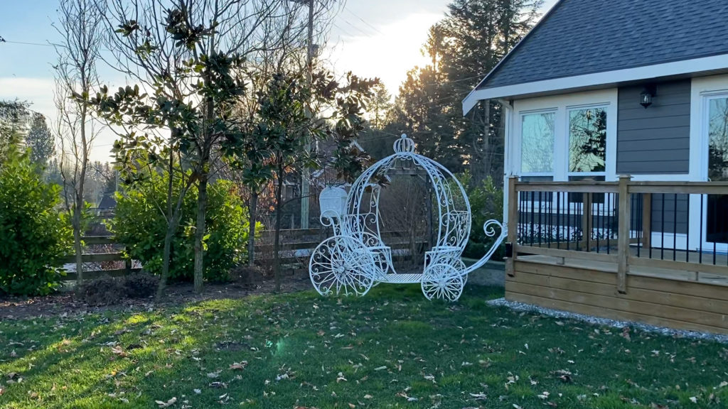 A white Cinderella style carriage sits on lush green grass by the guesthouse deck