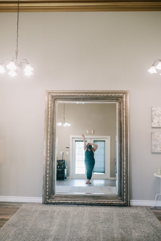 Megan in a green formal dress taking a selfie in the full length bridal suite mirror