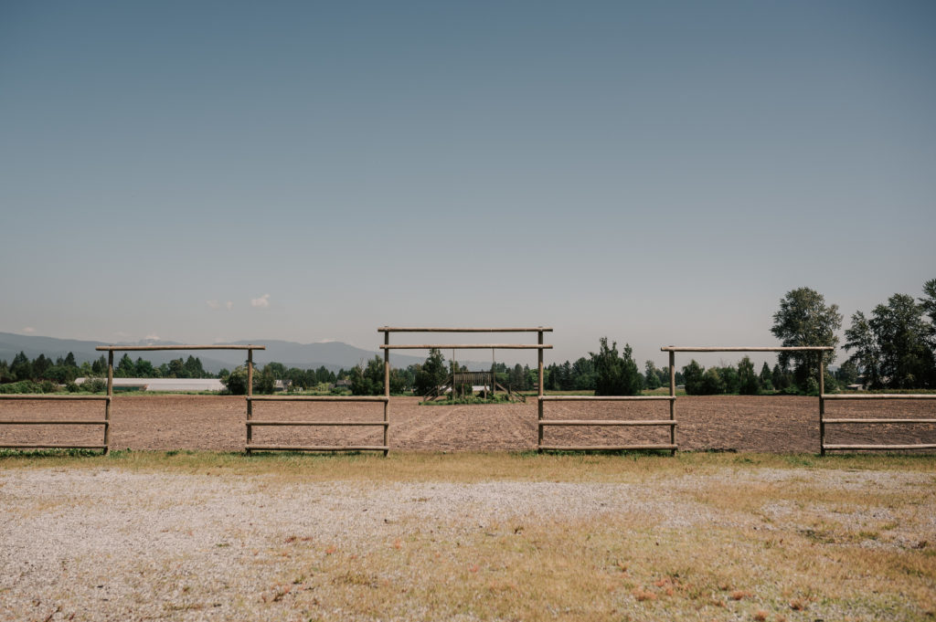 Three wooden farm style arches looking out to the fields in May. Later in the season, the fields will be filled with tall corn stalks.